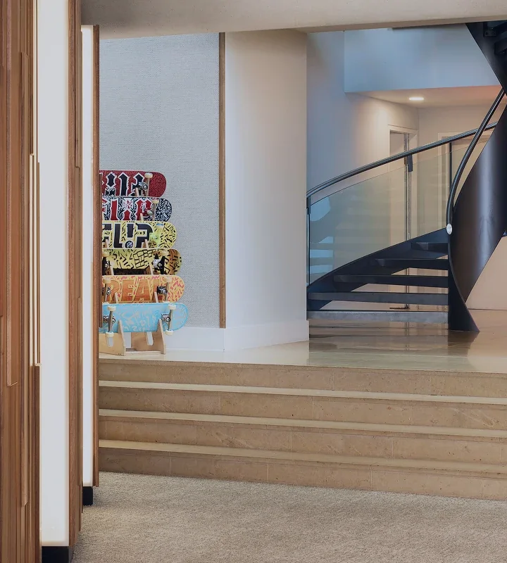 Sculptural black spiral staircase with glass balustrade beside a stacked skateboard-deck art installation in the Cheyne Capital Real Estate office